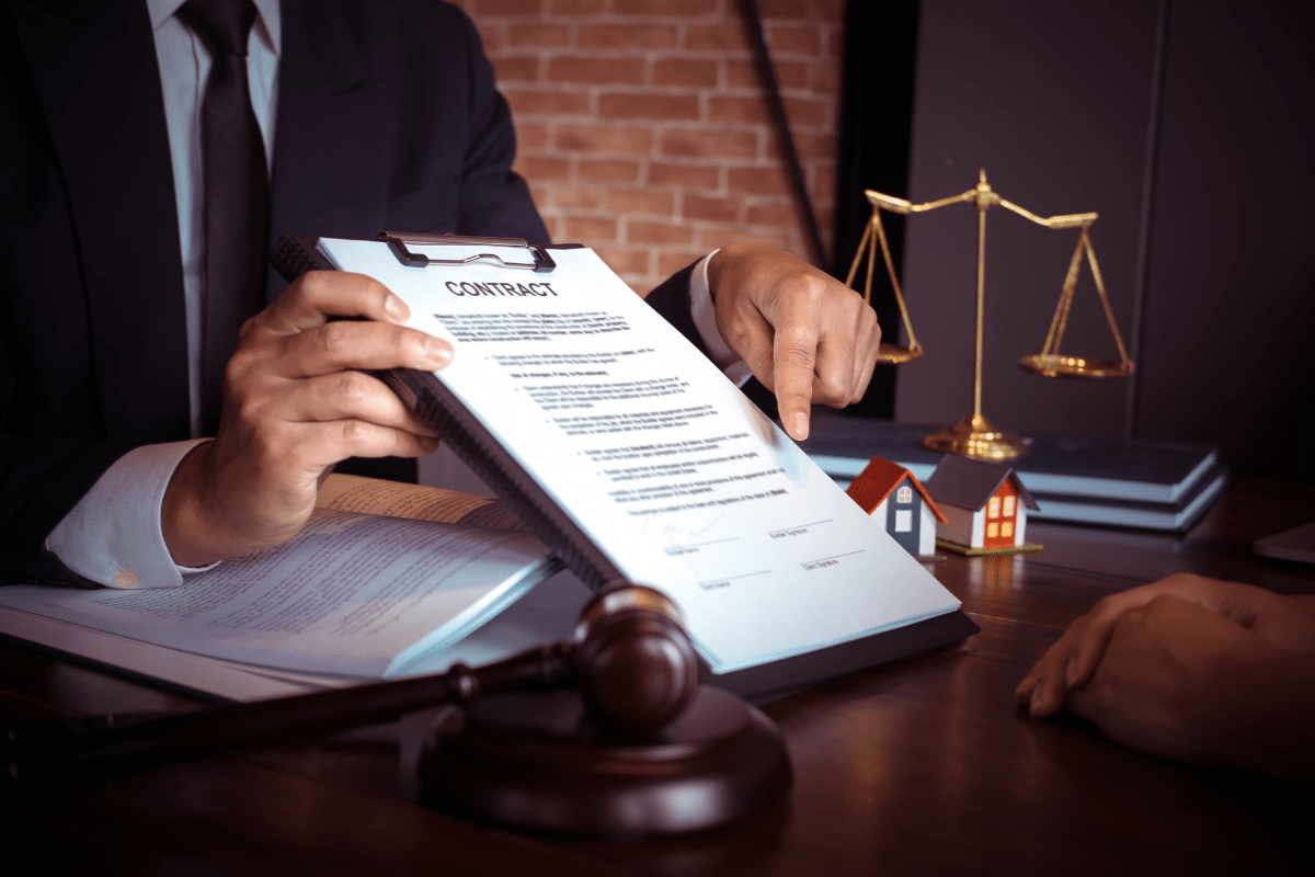 Anwalt erklärt Mietvertrag im Rahmen des Mietrechts, zeigt auf einen Vertragsordner, davor liegen Richterhammer Waage und kleine Hausmodelle auf dem Tisch