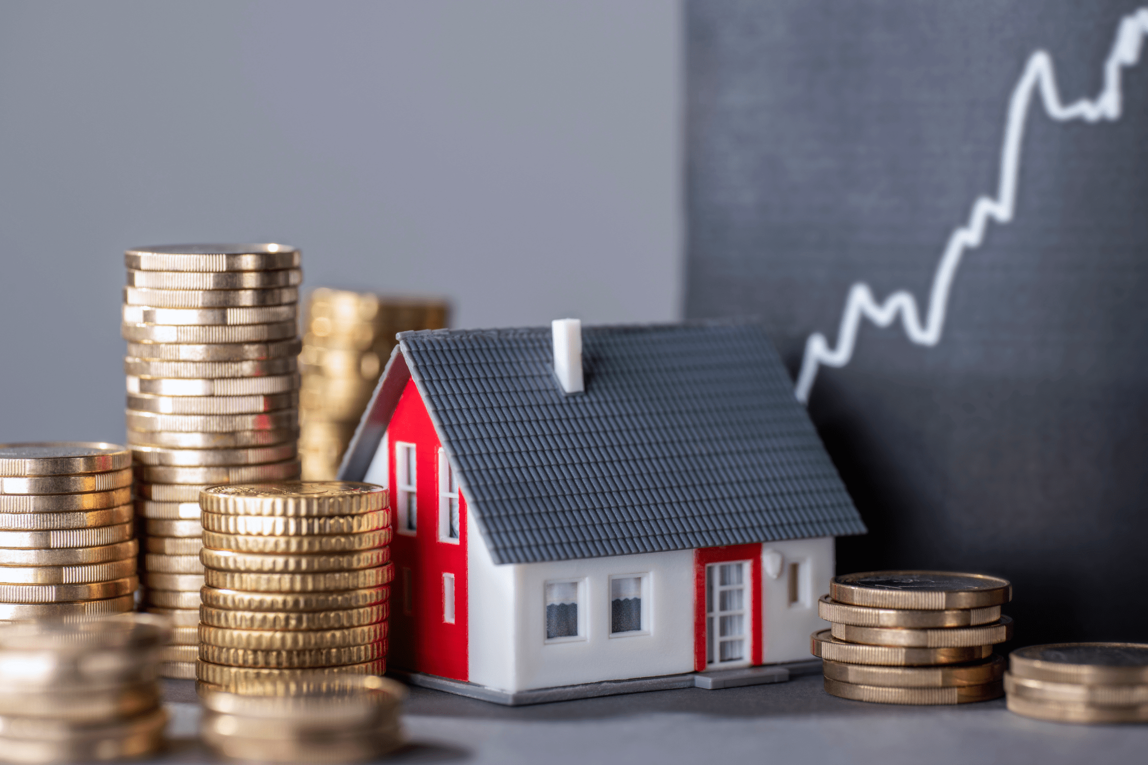 Symbolbild Immobilienwert: Miniaturhaus mit Münzstapeln und steigender Preiskurve – zeigt Entwicklung der Immobilienpreise und Kapitalrendite.