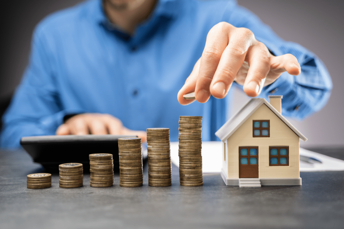 Immobilienpreise Österreich 2025 – Symbolbild mit Münzstapeln, Hausmodell und Berechnung der Investition