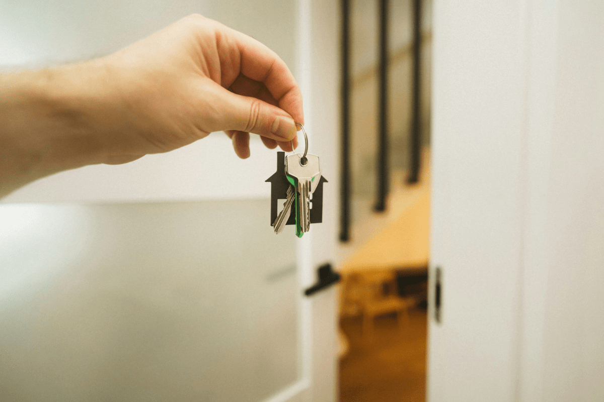 Wohnungskauf – Eine Hand mit einem Wohnungsschlüssel, offene Wohnungstür im Hintergrund